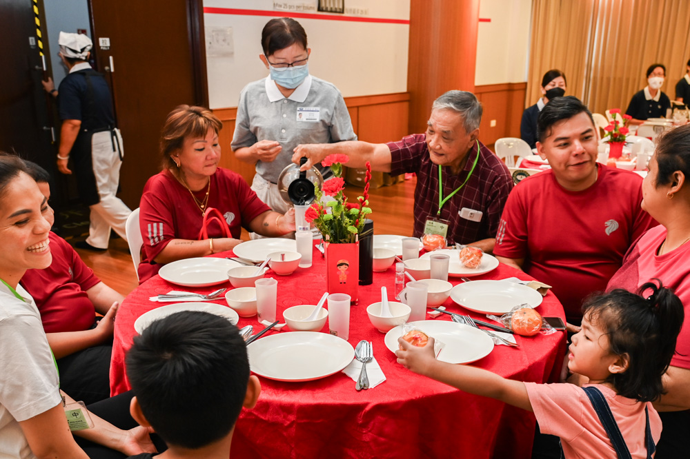 Tan Liang Chwee (third from right, holding a teapot), accompanied by his daughter Tan Wang Hoon (second from left) and their family of six attending the Lunar New Year Charity Distribution event. (Photo by Pua Poo Toong)